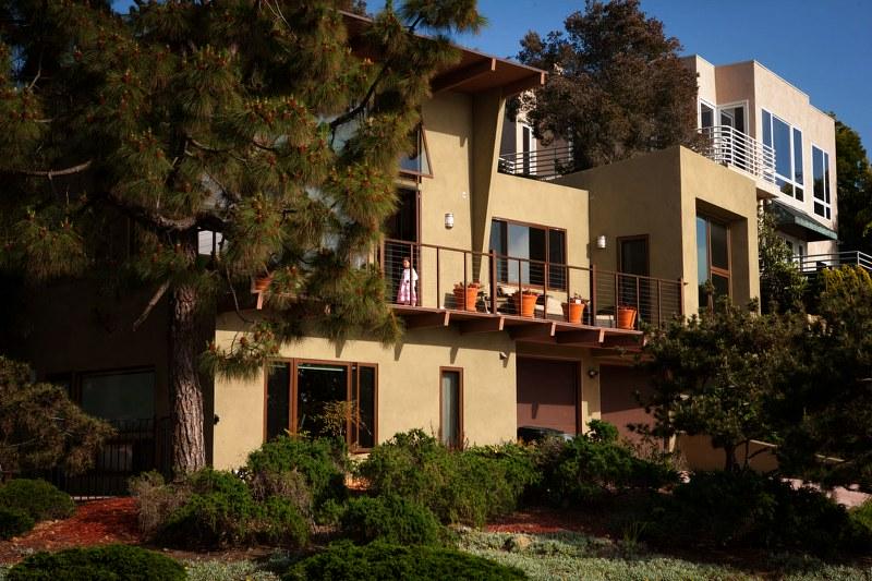 A large house with a balcony surrounded by green trees in a sunny setting.