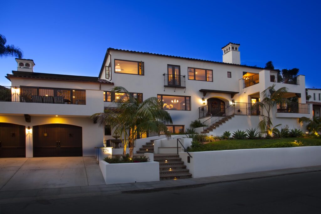 A large white house featuring a spacious driveway and prominent stairs leading to the entrance.