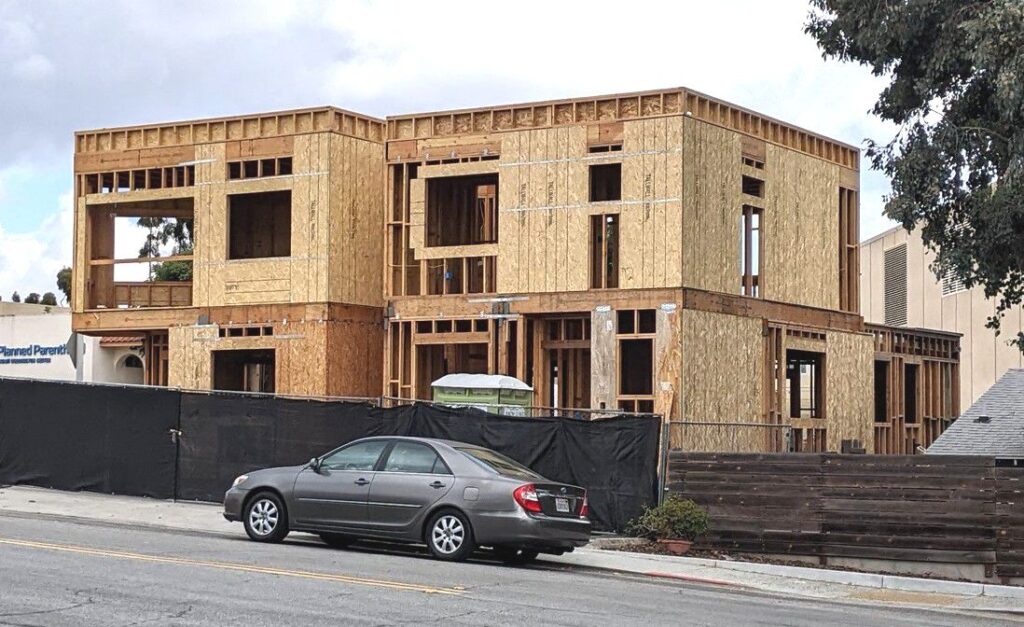 A parked car in front of a house that is currently under construction, with scaffolding and building materials visible.